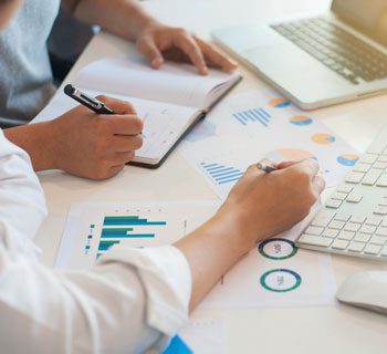 Two people reviewing financial data and take notes in a notebook.