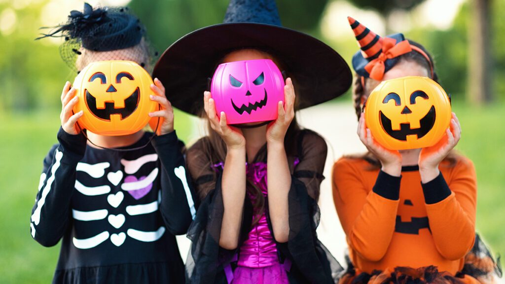 Kids in costumes hide their heads behind pumpkins buckets pumpkins