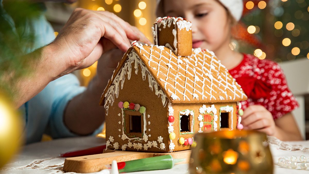 Father and daughter in red hat building gingerbread house.