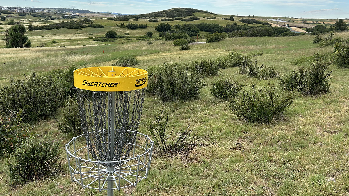A disc golf basket and surrounding hills at Pronghorn Park and Disc Golf Course.