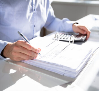 Businessperson Calculating Invoice Using Calculator At Desk