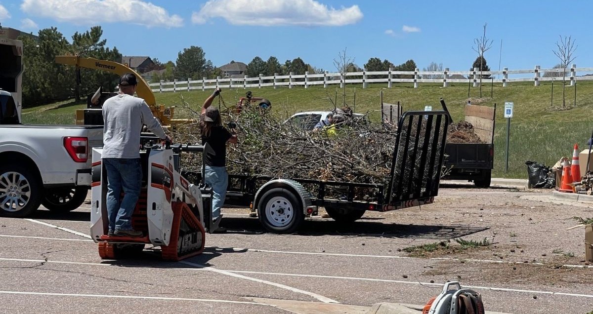 Two men load tree branches and brush onto a truck for removal.
