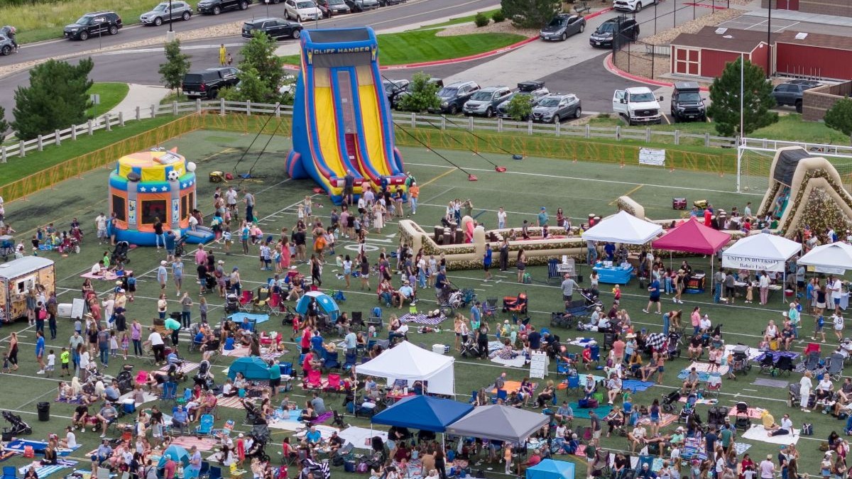 Large gathering of people on an outdoor field surrounded by an inflatable slide and pop up tents.