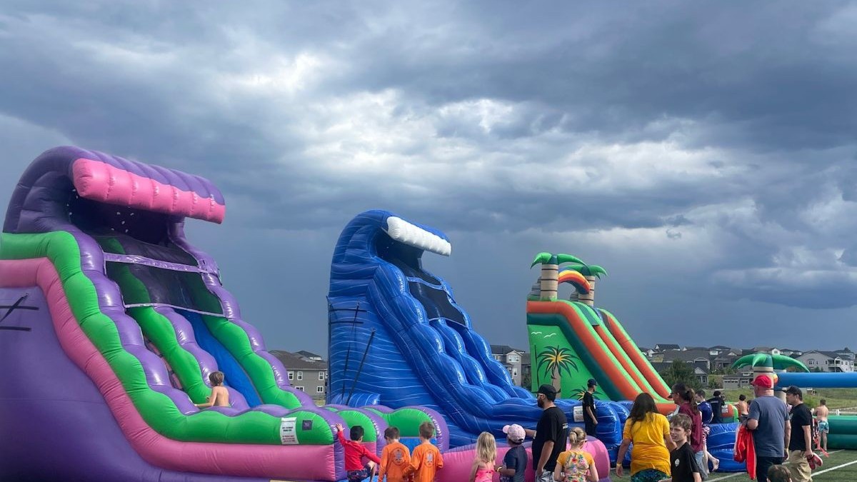 Kids lined up in front of three large inflatable water slides.