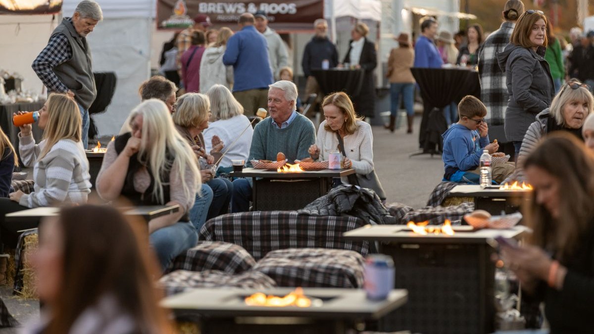 Several people gathered around tables with fires in the center for making smores.