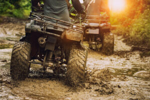 A man riding an ATV on off road dirt trail with the sun shining in the sky.